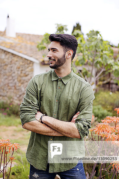 Thoughtful man smiling while standing arms crossed at yard