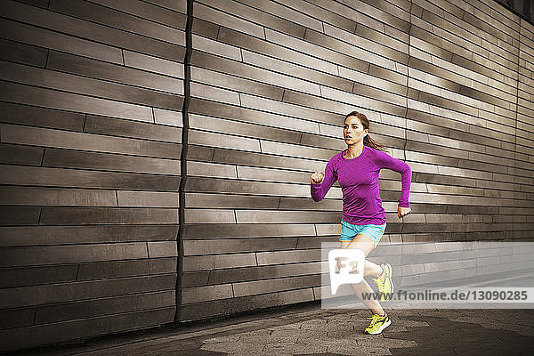 Frau joggt auf Bürgersteig an Wand