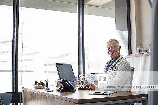 Portrait of smiling doctor working at desk by window in hospital