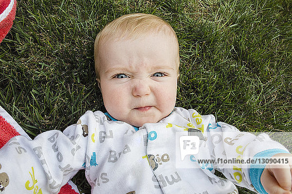 Portrait eines süßen kleinen Jungen  der ein Gesicht macht  während er auf einem Grasfeld im Hinterhof liegt