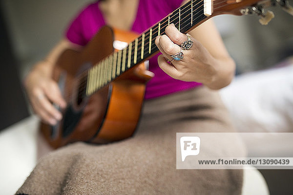 Midsection of woman playing guitar at home