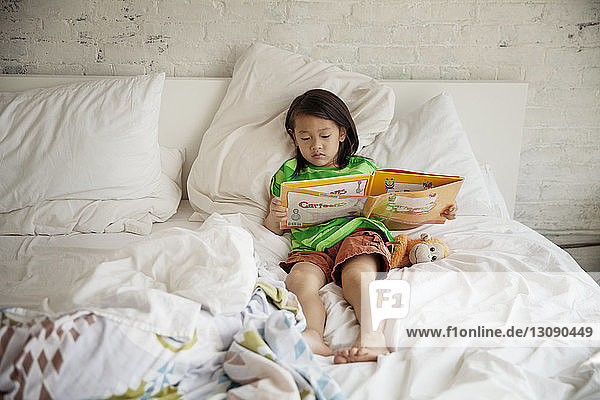 Mädchen liest Bilderbuch in voller Länge  während sie zu Hause auf dem Bett liegt