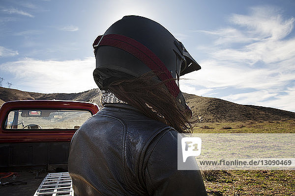 Rear view of female biker wearing helmet by pick-up truck on mountain against sky