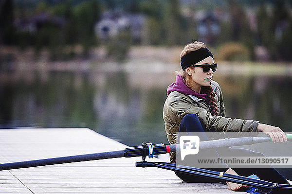 Young woman sitting on jetty with oar by lake