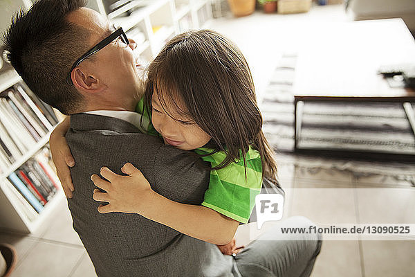 Hochwinkelaufnahme eines Vaters  der seine Tochter im hell erleuchteten Wohnzimmer zu Hause umarmt