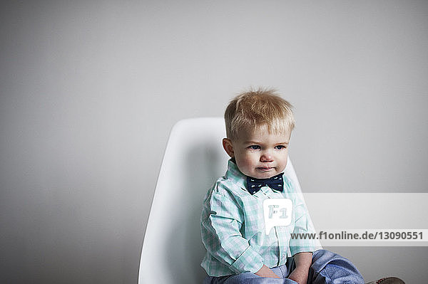 Trauriger kleiner Junge sitzt zu Hause auf einem Stuhl an einer weißen Wand
