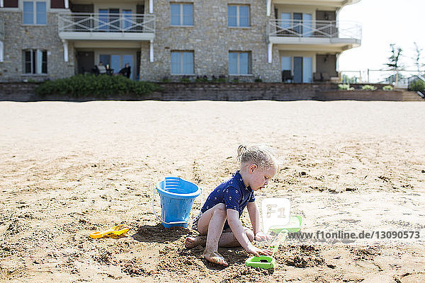 Girl playing with toys at sandy beach on sunny day