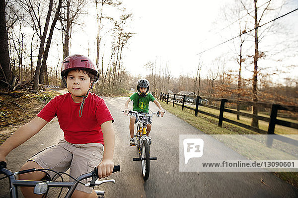 Brothers riding bicycles on road against clear sky
