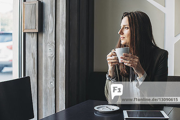 Thoughtful businesswoman holding coffee cup at cafe table