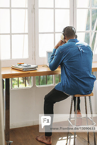 Full length rear view of man working at home office by window