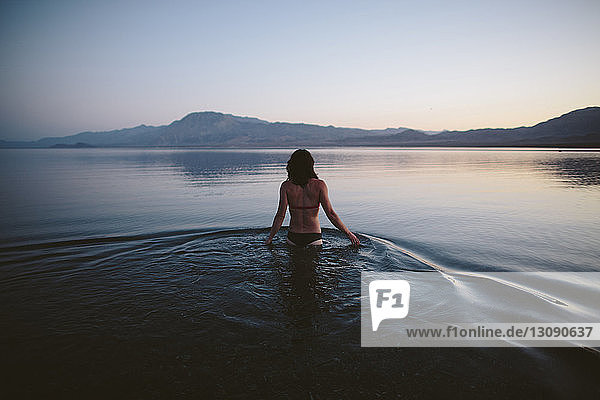 Rückansicht einer Frau im Bikini  die in der Dämmerung im See vor klarem Himmel steht