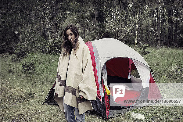 Woman wrapped in blanket standing outside tent against trees