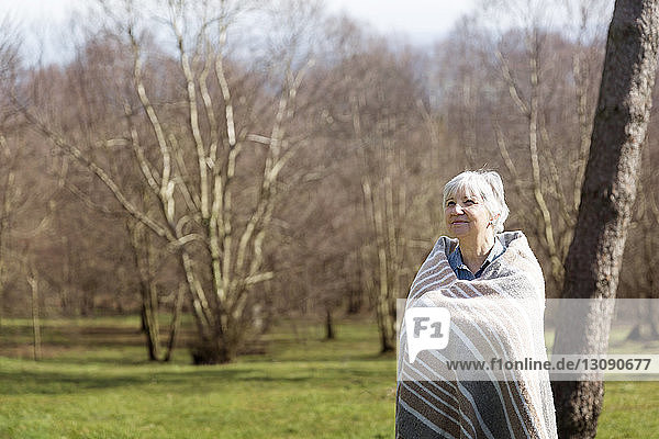 Nachdenkliche ältere Frau in eine Decke gehüllt  die im Winter auf dem Feld steht