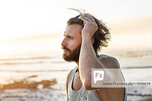 Seitenansicht eines nachdenklichen Mannes  der bei Sonnenuntergang am Strand seine Sonnenbrille einstellt