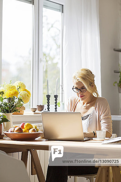 Frau benutzt Laptop-Computer  während sie am Tisch am Fenster sitzt