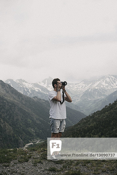 Man photographing while standing on mountain against sky