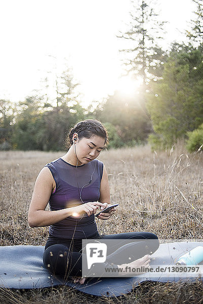Frau hört Musik  während sie ein Smartphone auf der Trainingsmatte auf dem Feld benutzt