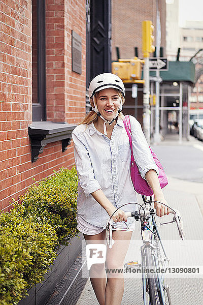 Glückliche Frau geht mit dem Fahrrad auf dem Bürgersteig in der Stadt