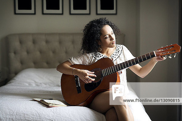 Frau justiert Gitarrenknoten  während sie auf dem Bett sitzt