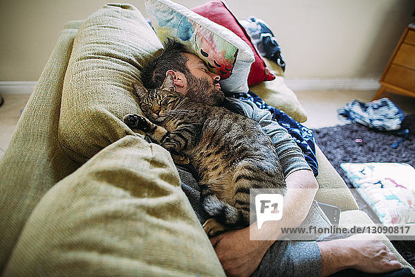 Hochwinkelansicht eines Mannes mit Katze  der zu Hause auf dem Sofa schläft