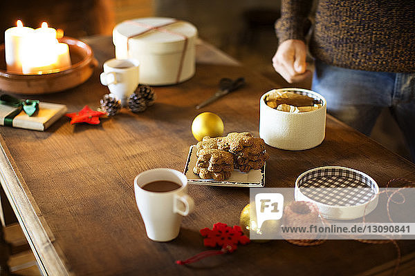 Ausgeschnittenes Bild eines Mannes  der einen Geschenkkarton vorbereitet  während er Kekse und Kaffee bei Tisch isst