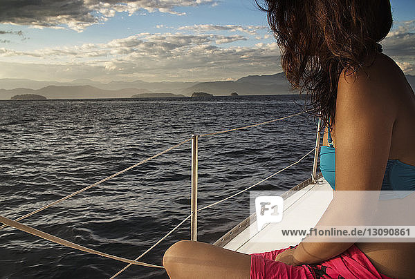 Frau sitzt bei Sonnenuntergang im Boot auf dem Meer gegen den Himmel