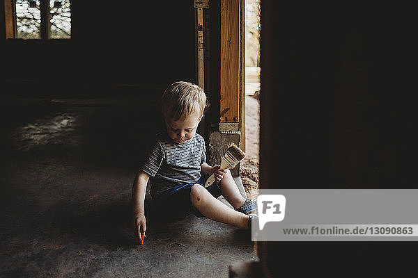 Kleiner Junge mit Bürste sitzt am Eingang in einem verlassenen Raum
