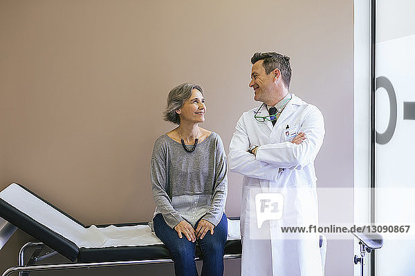 Lächelnder Patient schaut den Arzt an  während er im Krankenhaus im Bett an der Wand sitzt