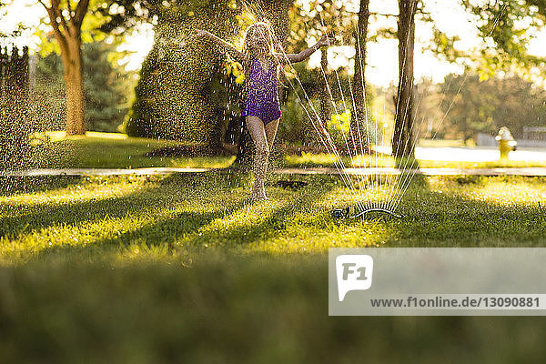 Happy girl playing in sprinkler at backyard