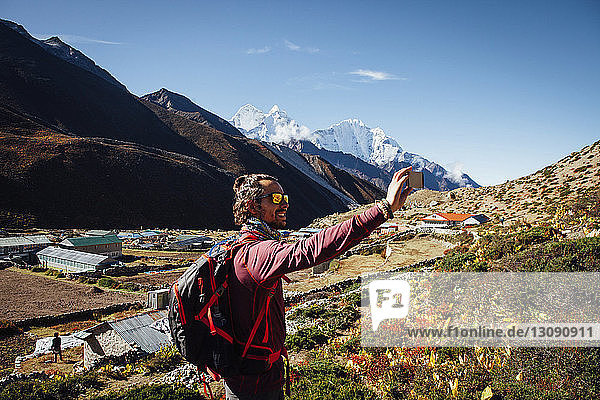 Male hiker taking selfie while standing on mountain against blue sky at Sagarmatha National Park