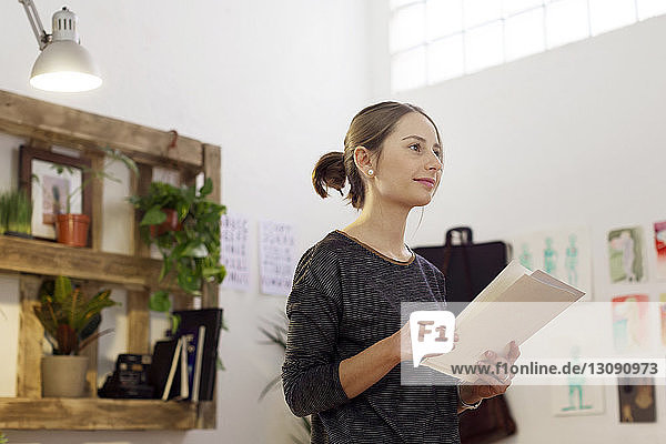 Thoughtful female illustrator looking away while holding papers in creative office