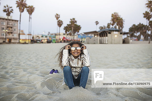Happy girl wearing sunglasses while sitting on sand at beach