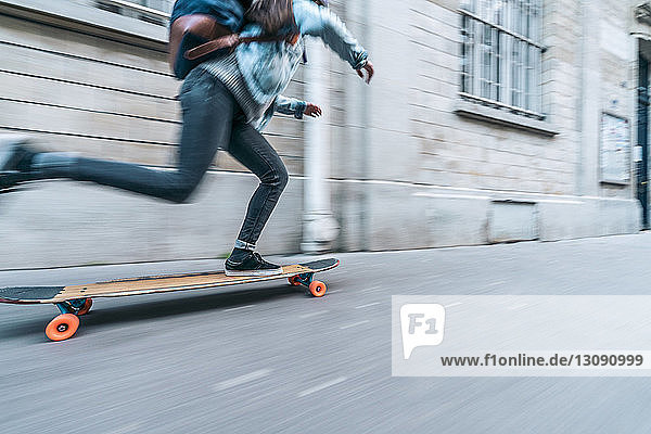 Verschwommene Bewegung von Skateboard fahrenden Frauen auf einem Fußweg durch ein Gebäude in der Stadt