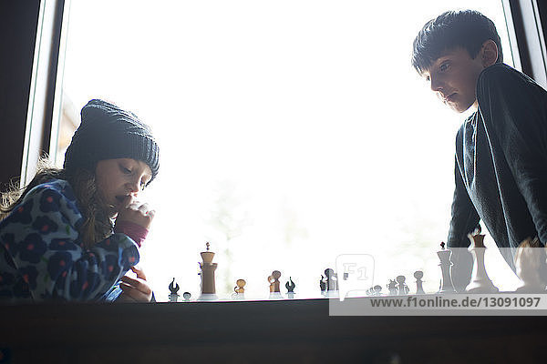 Niedrigwinkelansicht von Geschwistern  die zu Hause am Fenster Schach spielen