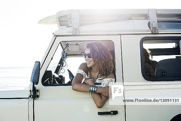 Lächelnde Frau mit Sonnenbrille sitzt bei Sonnenschein im Geländewagen