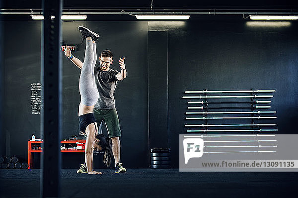 Fitness instructor assisting woman in doing handstand in gym