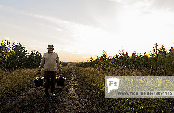 Man holding mushrooms in buckets while standing on dirt road at field against sky