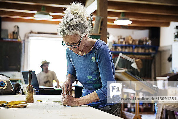 Handwerkerin beim Formen von Holz mit dem Meißel bei Tisch in der Werkstatt