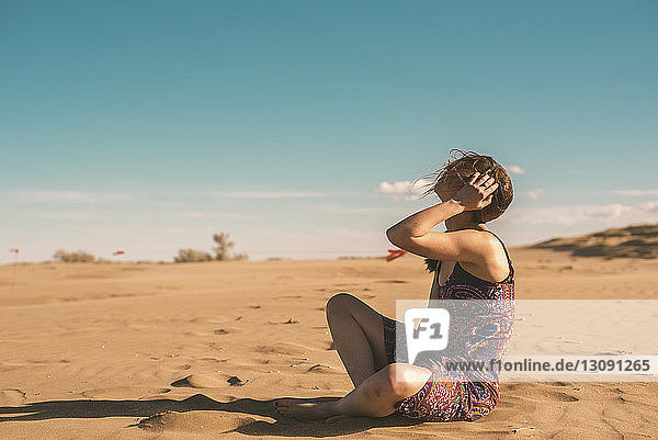 Seitenansicht einer Frau  die am Strand im Sand vor blauem Himmel am sonnigen Tag sitzt