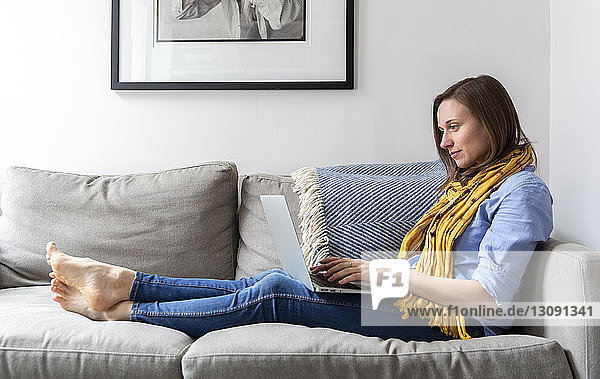 Seitenansicht einer Frau  die einen Laptop-Computer benutzt  während sie auf dem Sofa im Wohnzimmer sitzt