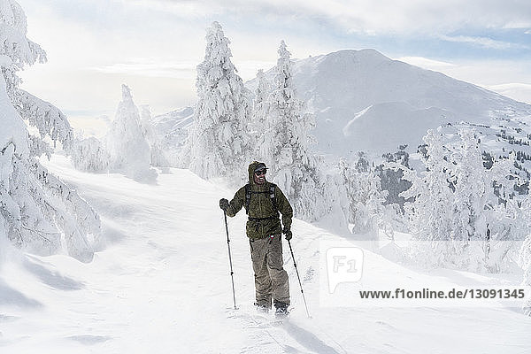 Mann in voller Länge mit Skiausrüstung steht bei nebligem Wetter auf schneebedecktem Berg