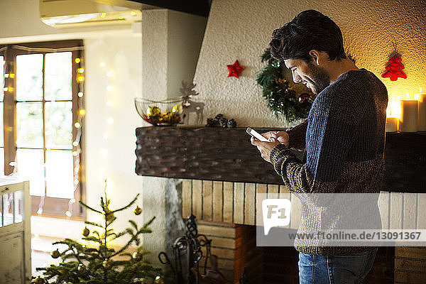Lächelnder Mann benutzt Smartphone  während er zu Weihnachten zu Hause steht