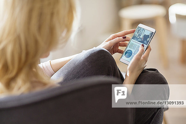 Woman using mobile phone while relaxing on armchair