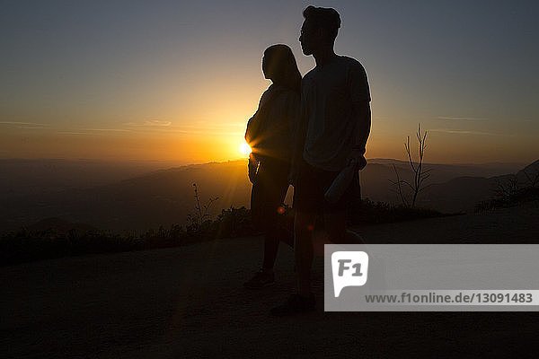 Silhouettenpaar steht bei Sonnenuntergang auf Berg gegen Himmel