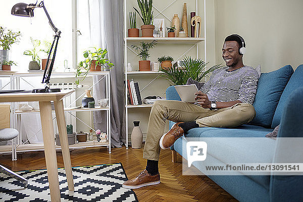 Glücklicher Mann benutzt Tablet-Computer  während er zu Hause auf dem Sofa sitzt