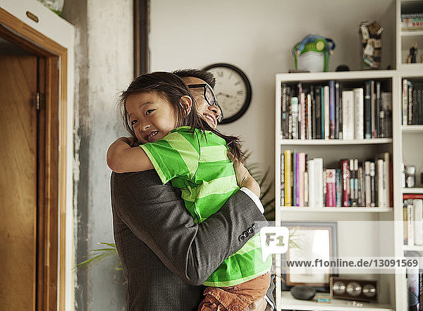 Glücklicher Vater umarmt Tochter  während er zu Hause im Wohnzimmer steht