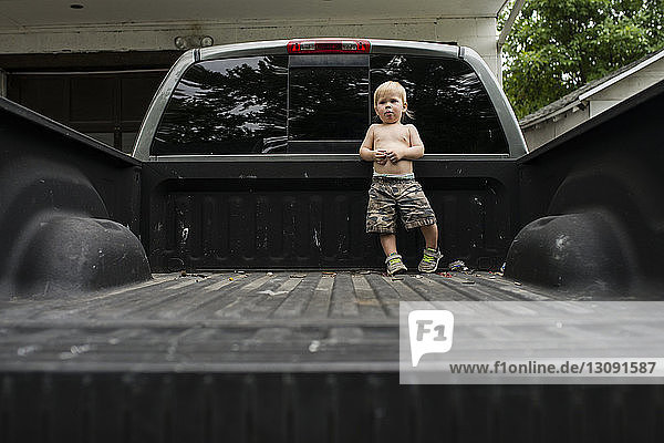 Boy looking away while standing on pick-up truck