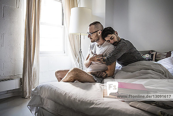 Zärtliches schwules Paar  das zu Hause auf dem Bett sitzt