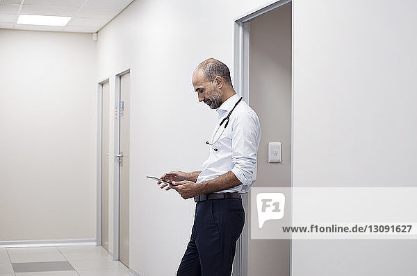 Side view of doctor using tablet computer while standing by door in corridor