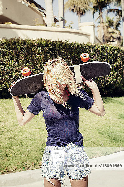 Frau trägt Skateboard auf den Schultern am Fussweg